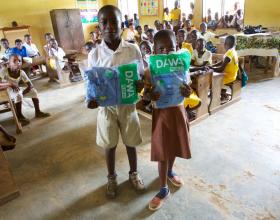 Source - © 2016 Sarah Hoibak/VectorWorks, Courtesy of Photoshare. Addo and Festus, students at Amanhyia Catholic School in Ghana, receive long-lasting insecticide-treated bed nets (LLINs) from their teacher Justine Ayivor during the 2016 Ghana Primary School based distribution campaign.