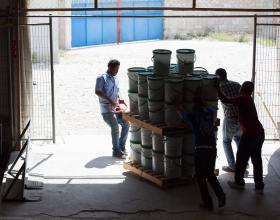 People moving a pallet of filled buckets out of a building.