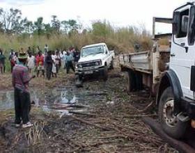 Residents gather as supply and service delivery trucks navigate a washed-out road in Ile district, Mozambique.