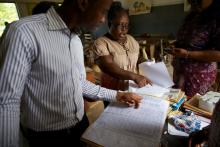 Eric, the monitoring and evaluation (M&E) officer for the VectorWorks program, discusses the registration of students with the School Health Education Program Coordinator for Effutu Municipality and a teacher at the Don Bosco Primary School. © 2016 Sarah Hoibak/VectorWorks, Courtesy of Photoshare. People reviewing documents