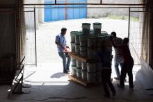 People moving a pallet of filled buckets out of a building.